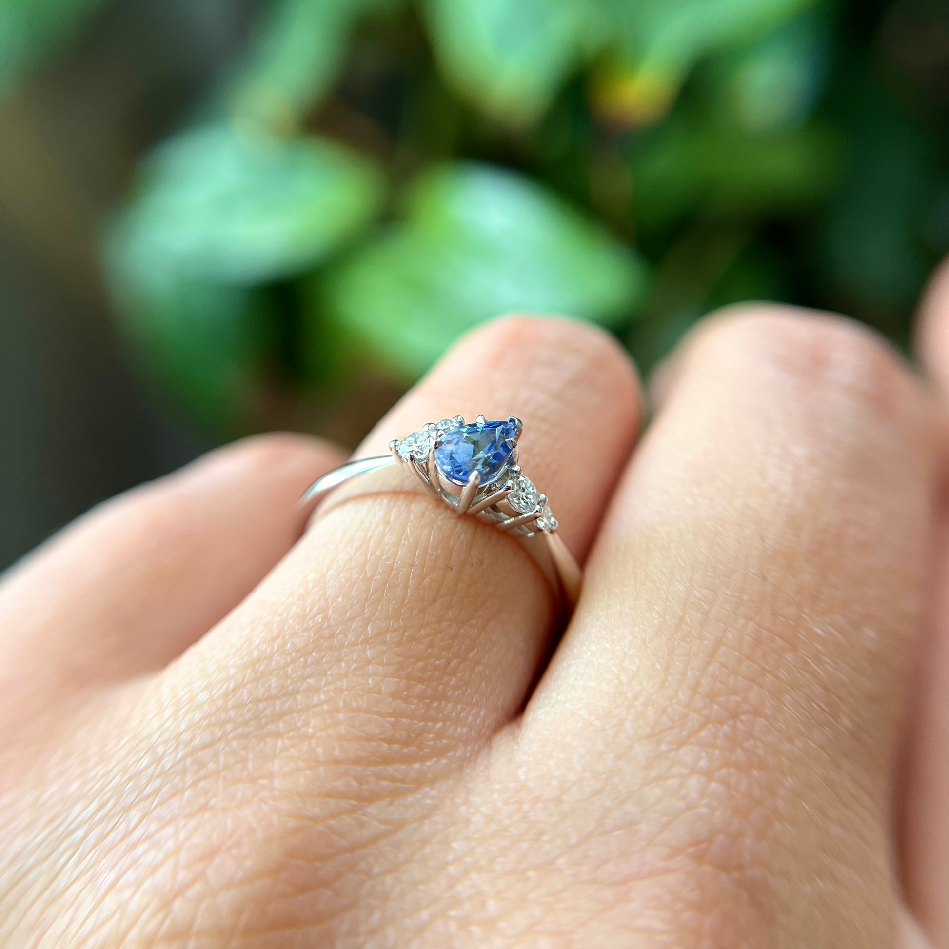 Bague de fiançailles en saphir bleu taille poire de 0,52ct du Sri Lanka et diamants naturels en or blanc 14k, vue de côté portée au doigt montrant le profil du corps de bague et la hauteur du serti