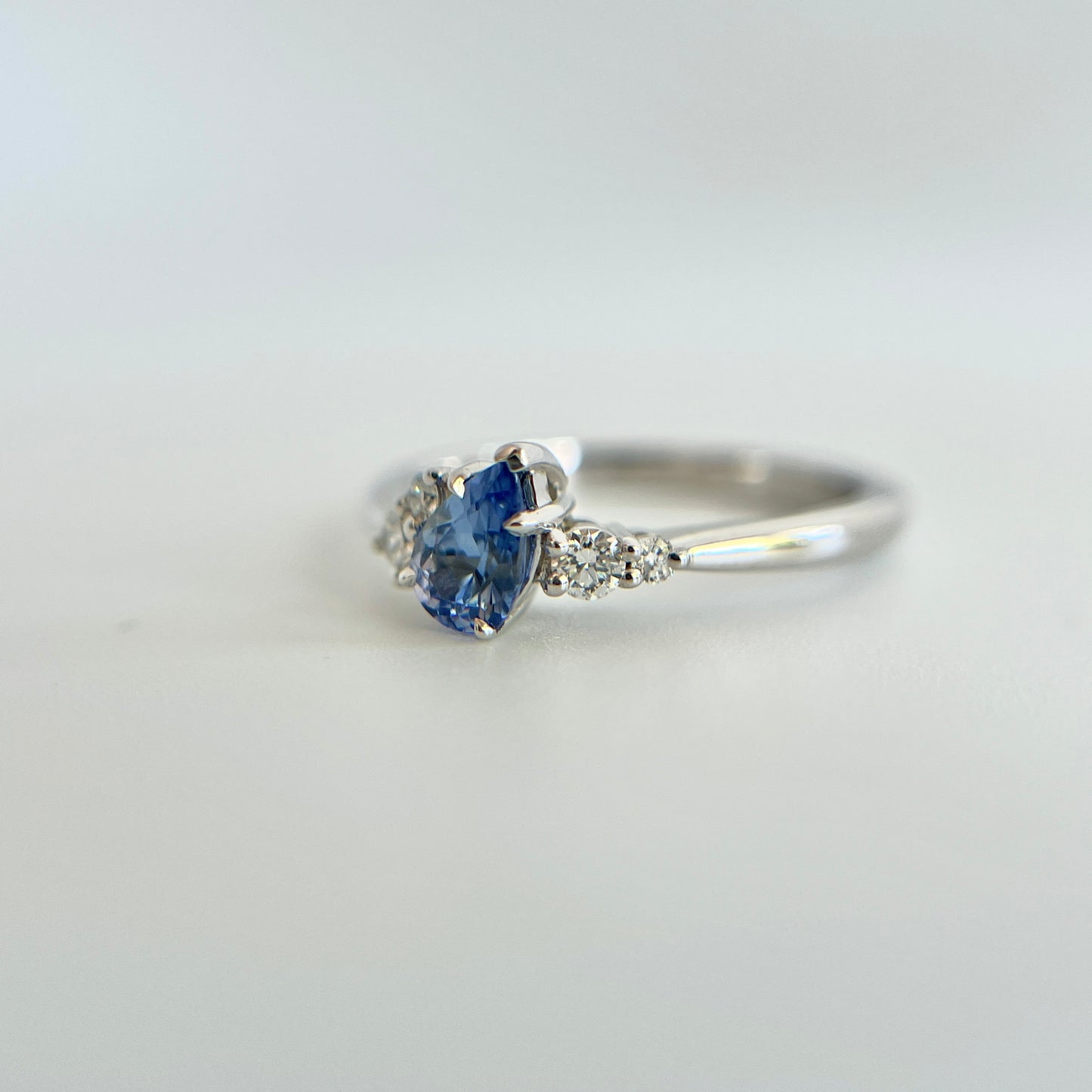 Bague de fiançailles en saphir bleu taille poire de 0,52ct du Sri Lanka et diamants naturels en or blanc 14k, vue en trois-quarts montrant la pierre inclinée et le détail du serti asymétrique