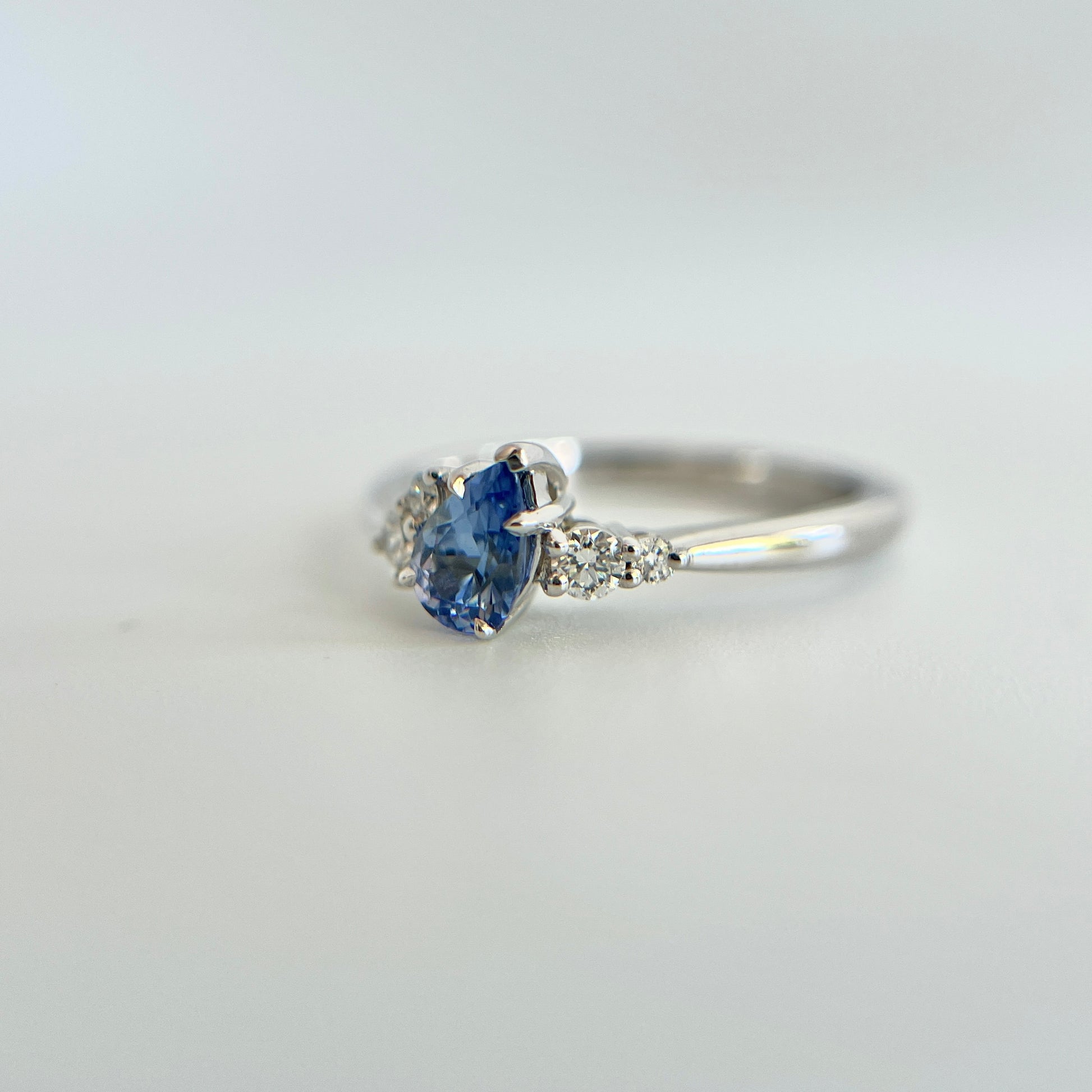 Bague de fiançailles en saphir bleu taille poire de 0,52ct du Sri Lanka et diamants naturels en or blanc 14k, vue en trois-quarts montrant la pierre inclinée et le détail du serti asymétrique