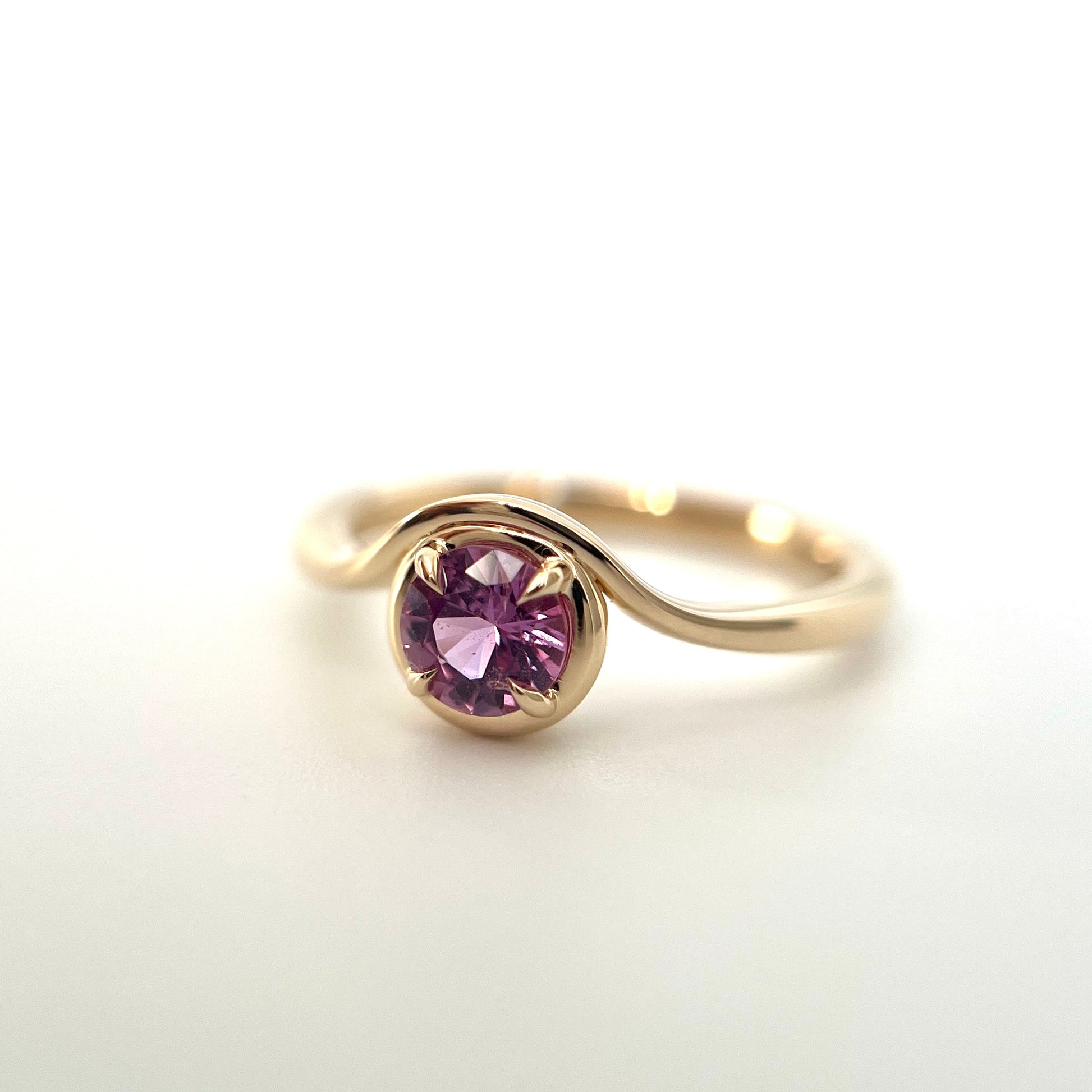 Pink sapphire solitaire ring in 14k yellow gold, side view showing wave band and setting detail