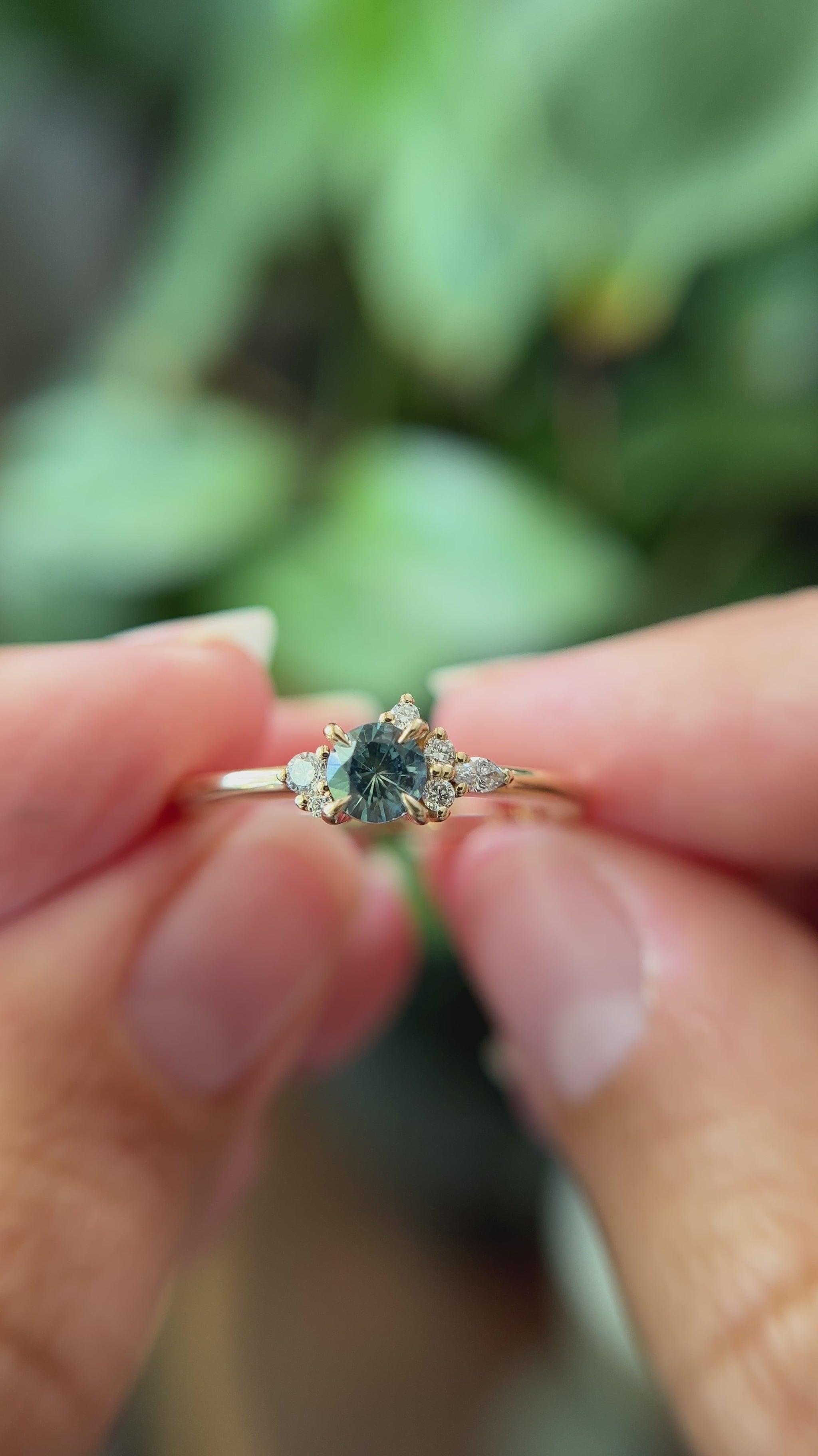 0.38ct round teal sapphire and natural diamond constellation engagement ring in 14k yellow gold, held in hands showing gemstone colour and faceting