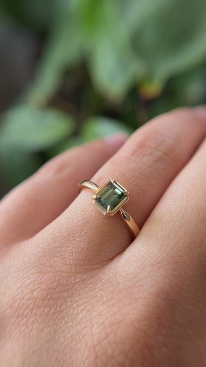 1.05ct emerald-cut forest green Madagascar sapphire solitaire engagement ring in 14k yellow gold, worn on finger showing colour and setting detail