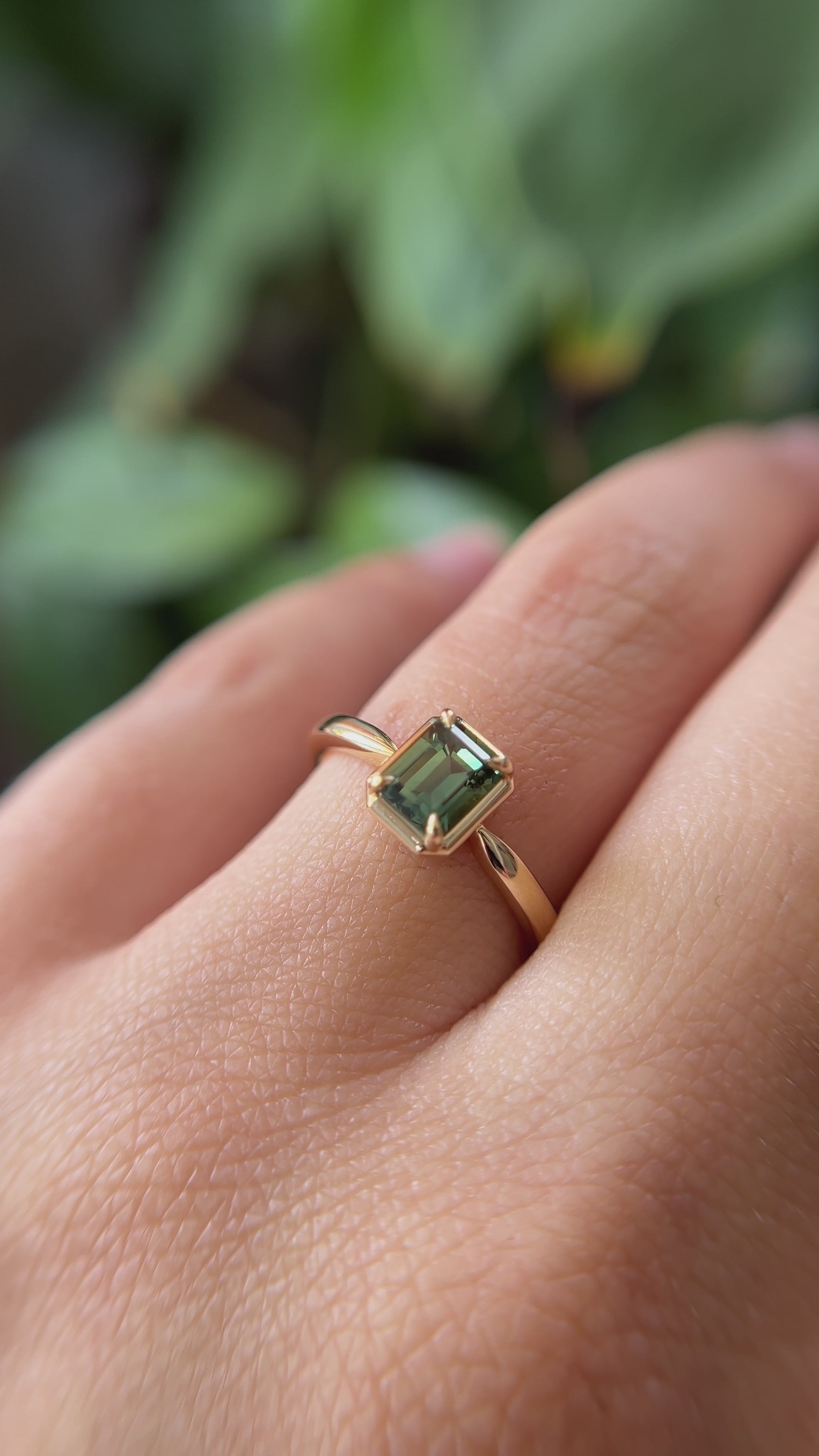 1.05ct emerald-cut forest green Madagascar sapphire solitaire engagement ring in 14k yellow gold, worn on finger showing colour and setting detail
