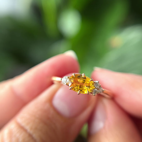 1.05ct oval bright yellow Sri Lankan sapphire and diamond ring in 14k yellow gold, held in hands showing stone colour and asymmetric diamond accents in motion