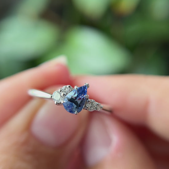 0.52ct pear shape blue Sri Lanka sapphire and natural diamond cluster engagement ring in 14k white gold, held in hands showing gemstone colour and faceting