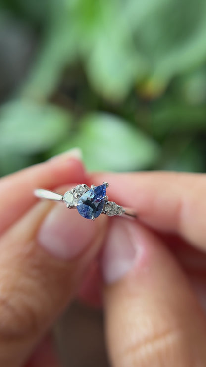 0.52ct pear shape blue Sri Lanka sapphire and natural diamond cluster engagement ring in 14k white gold, held in hands showing gemstone colour and faceting