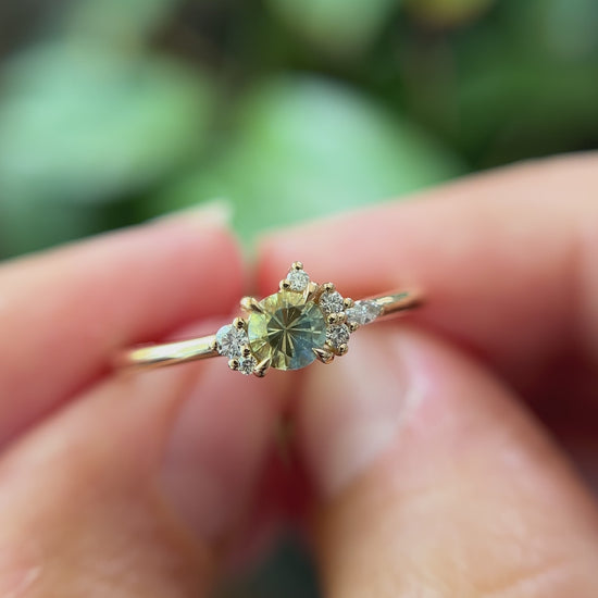 0.36ct round bi-color yellow to blue sapphire and natural diamond constellation engagement ring in 14k yellow gold, held in hands showing gemstone colour shift and faceting