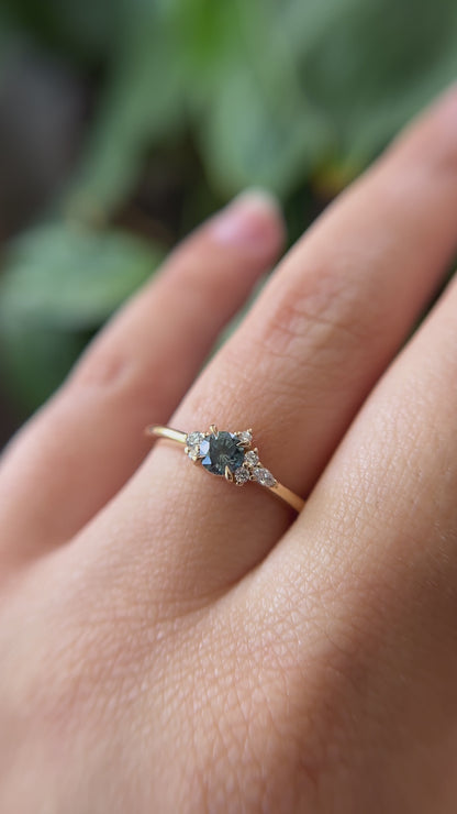 0.38ct round teal sapphire and natural diamond constellation engagement ring in 14k yellow gold, worn on finger showing gemstone colour and diamond cluster detail