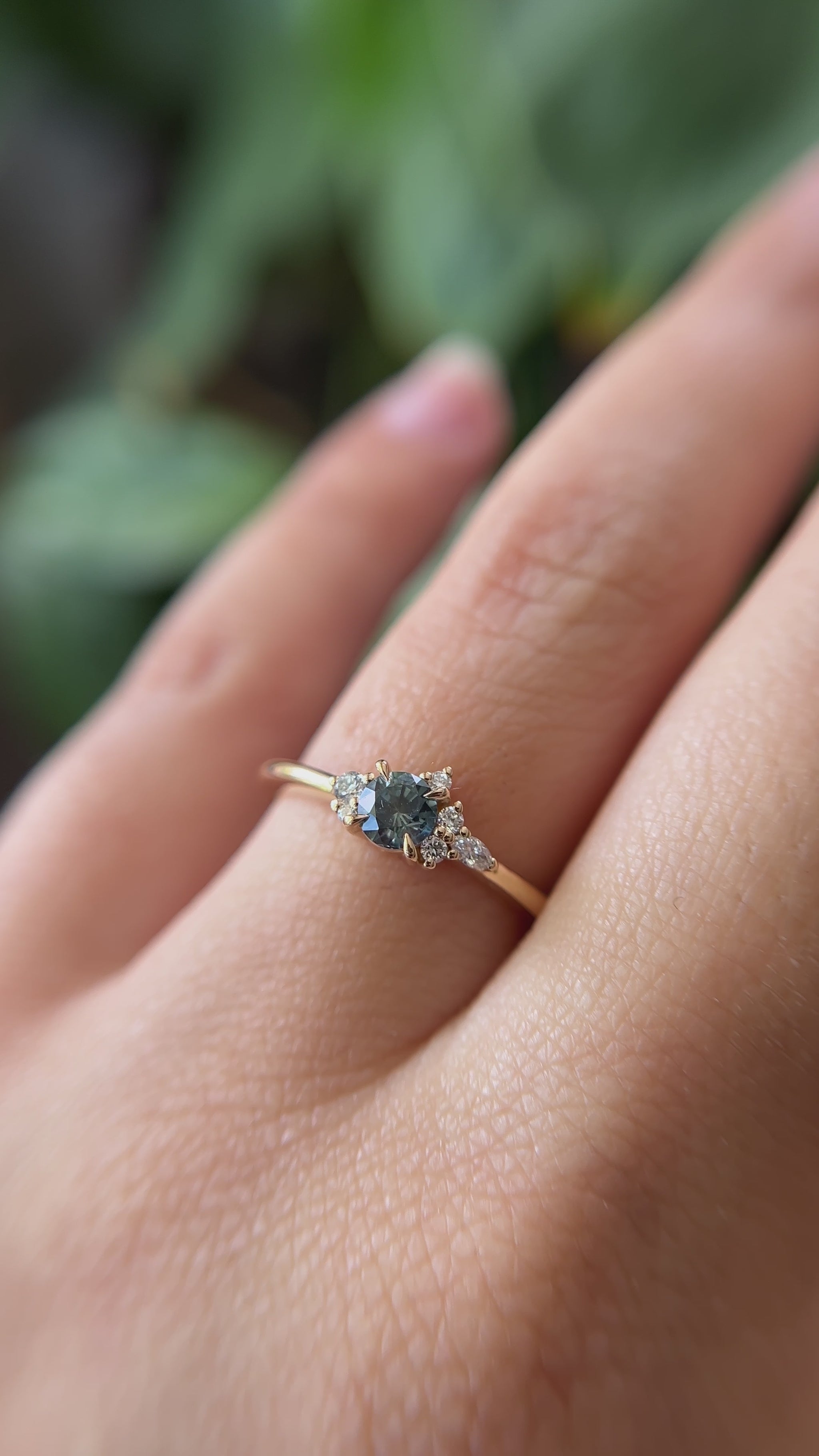 0.38ct round teal sapphire and natural diamond constellation engagement ring in 14k yellow gold, worn on finger showing gemstone colour and diamond cluster detail