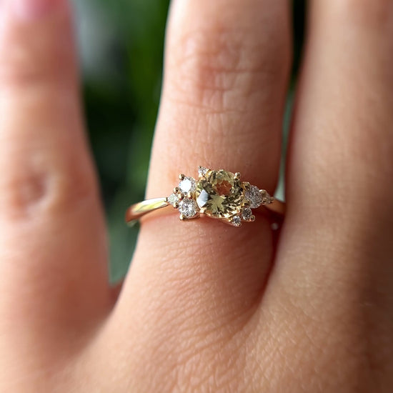 0.83ct round light yellow unheated Sri Lankan sapphire and diamond cluster engagement ring in 14k yellow gold, worn on hand showing stone colour and asymmetric diamond setting in motion