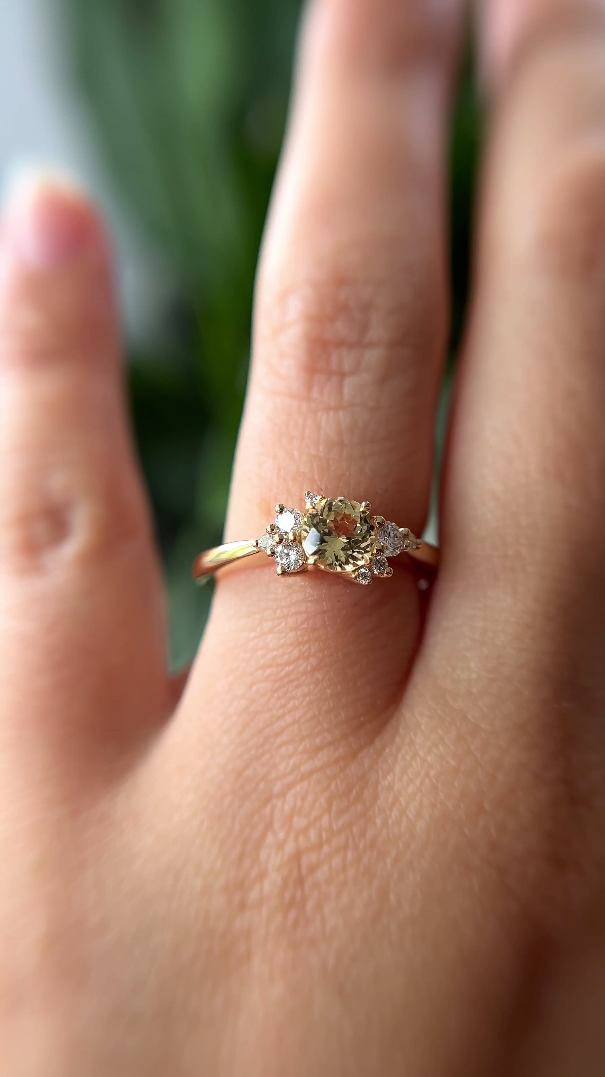 0.83ct round light yellow unheated Sri Lankan sapphire and diamond cluster engagement ring in 14k yellow gold, worn on hand showing stone colour and asymmetric diamond setting in motion