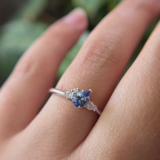 0.52ct pear shape blue Sri Lanka sapphire and natural diamond cluster engagement ring in 14k white gold, worn on finger showing tilted gemstone and diamond cluster detail