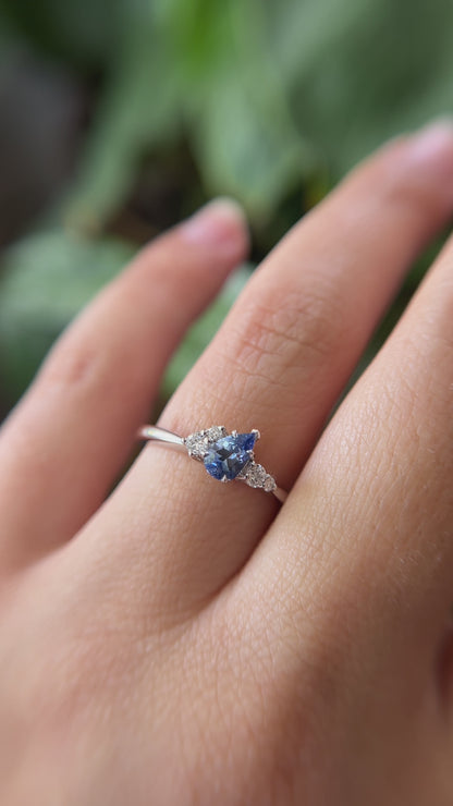 0.52ct pear shape blue Sri Lanka sapphire and natural diamond cluster engagement ring in 14k white gold, worn on finger showing tilted gemstone and diamond cluster detail