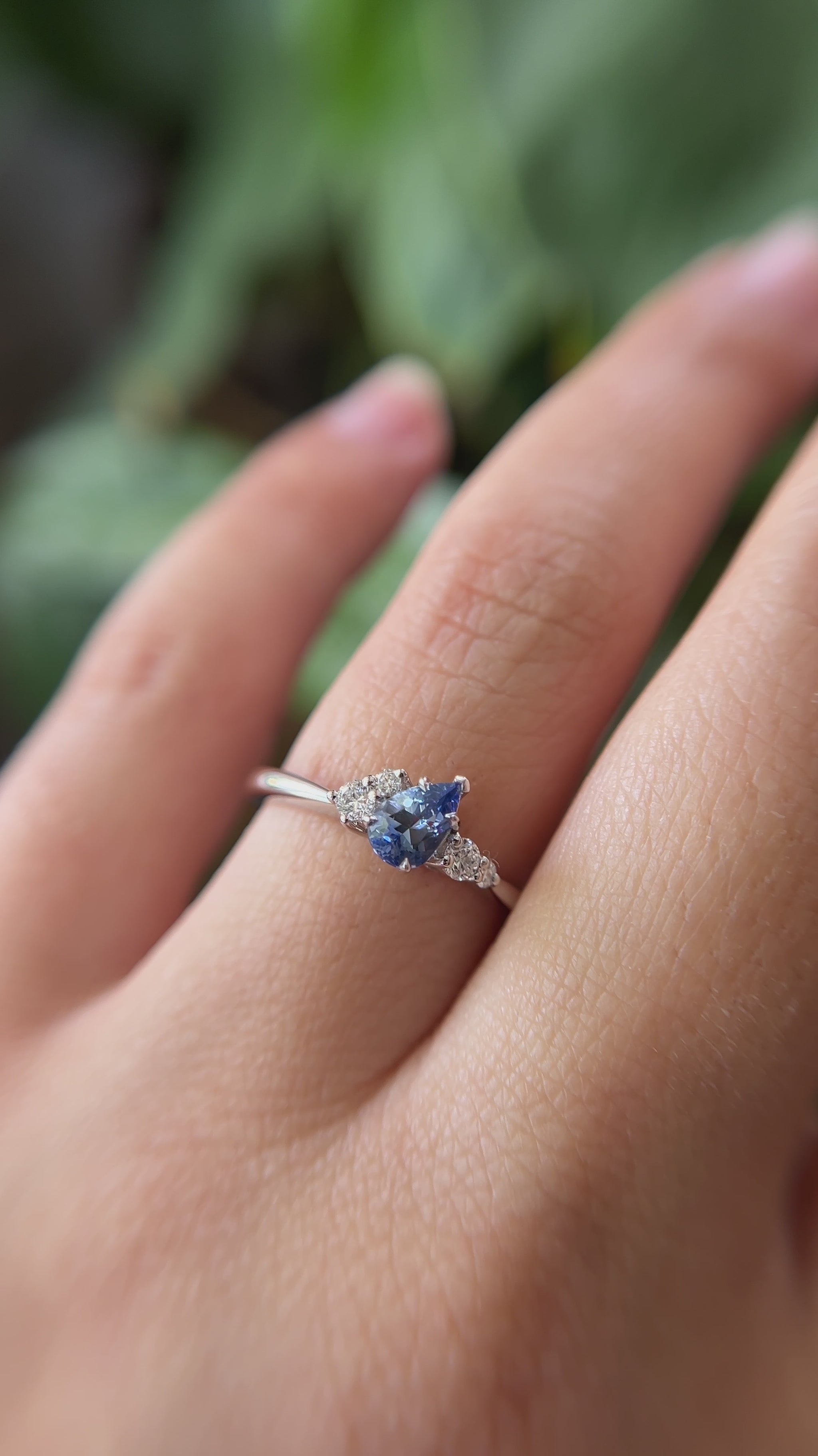 0.52ct pear shape blue Sri Lanka sapphire and natural diamond cluster engagement ring in 14k white gold, worn on finger showing tilted gemstone and diamond cluster detail