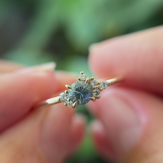 0.39ct round blue-teal sapphire and natural diamond constellation engagement ring in 14k yellow gold, held in hands showing gemstone colour and faceting