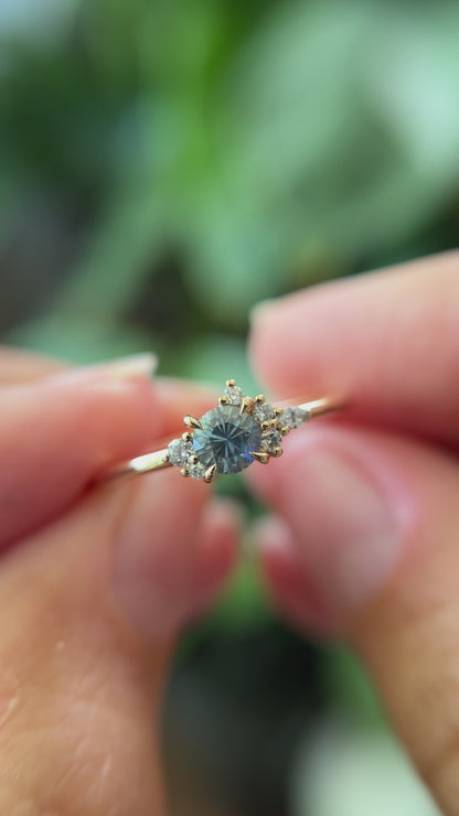 0.39ct round blue-teal sapphire and natural diamond constellation engagement ring in 14k yellow gold, held in hands showing gemstone colour and faceting