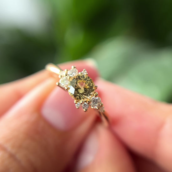 0.83ct round light yellow unheated Sri Lankan sapphire and diamond cluster engagement ring in 14k yellow gold, held in hands showing stone colour and asymmetric diamond setting in motion