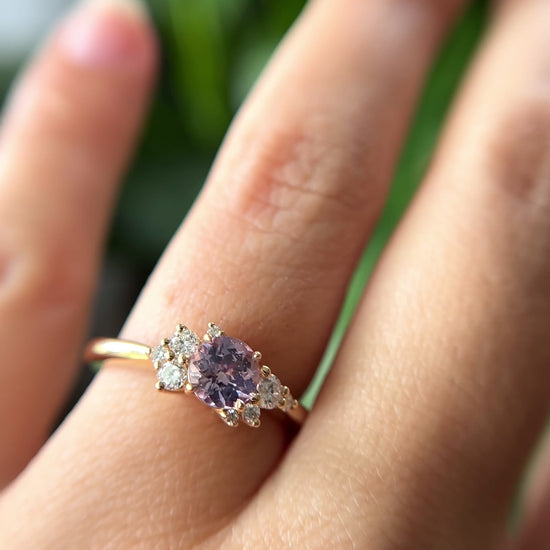 0.83ct round light purple unheated Sri Lankan sapphire and diamond cluster engagement ring in 14k yellow gold, worn on hand showing stone colour and asymmetric diamond setting in motion