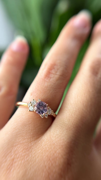 0.83ct round light purple unheated Sri Lankan sapphire and diamond cluster engagement ring in 14k yellow gold, worn on hand showing stone colour and asymmetric diamond setting in motion