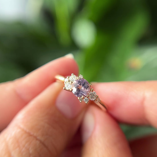 0.83ct round light purple unheated Sri Lankan sapphire and diamond cluster engagement ring in 14k yellow gold, held in hands showing stone colour and asymmetric diamond setting in motion