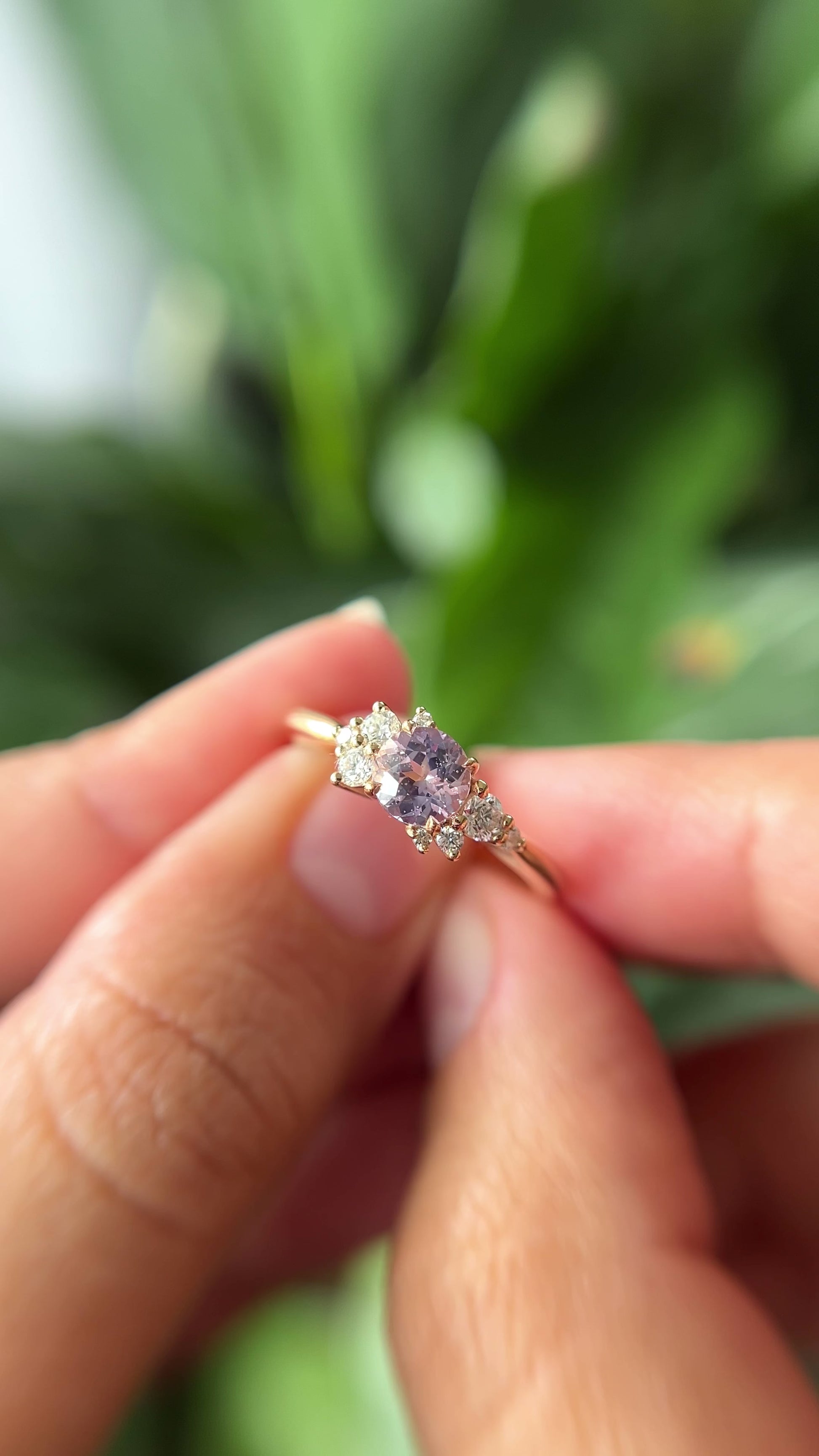 0.83ct round light purple unheated Sri Lankan sapphire and diamond cluster engagement ring in 14k yellow gold, held in hands showing stone colour and asymmetric diamond setting in motion
