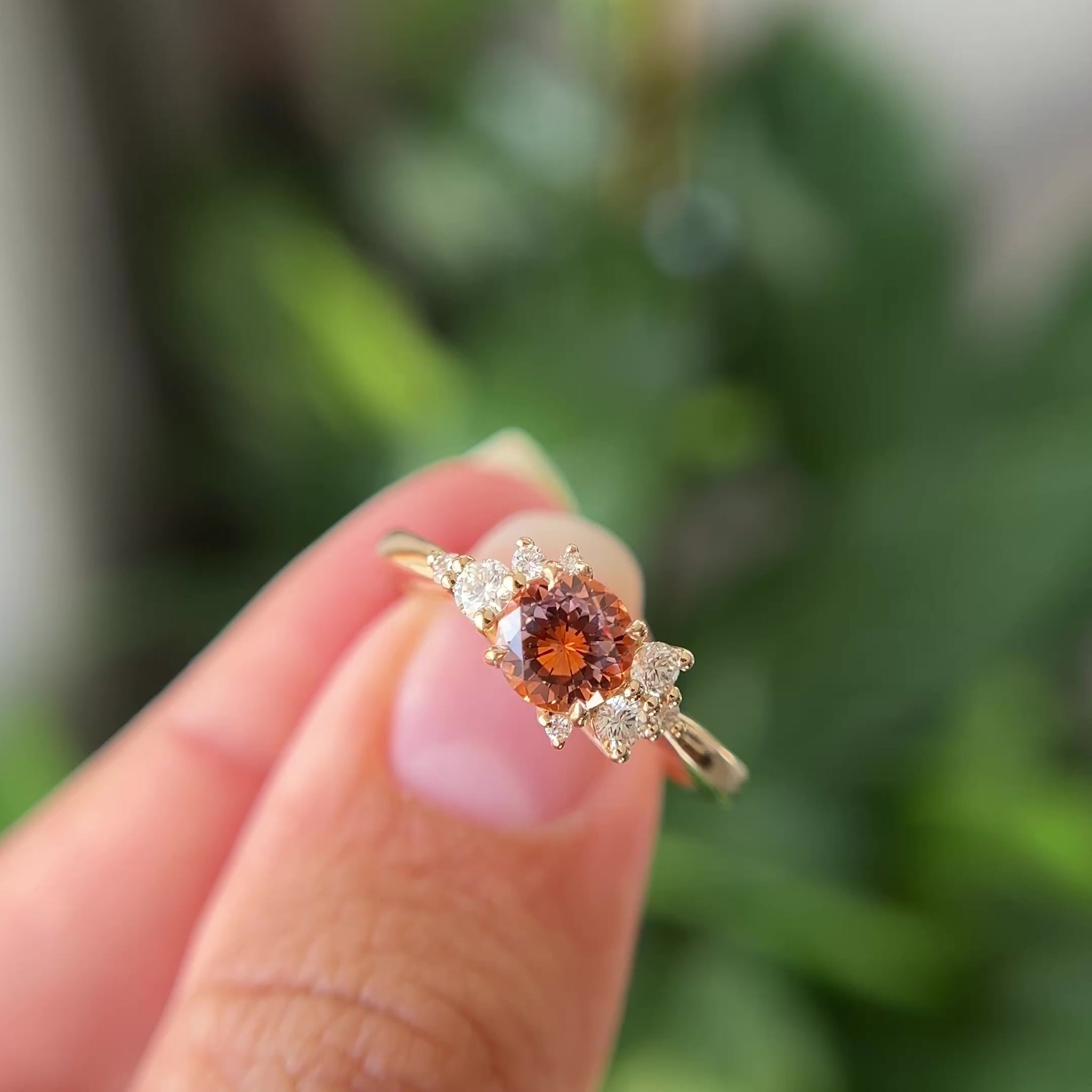 Orange-pink Montana sapphire and diamond cluster ring in 14k yellow gold, showing colour shift from orange to pink-purple in motion
