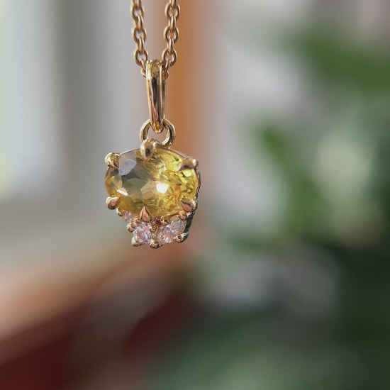 14k yellow gold pendant, set with a oval golden beryl and natural diamond accents. The pendant is hanging from a chain, in front of a green blurry background