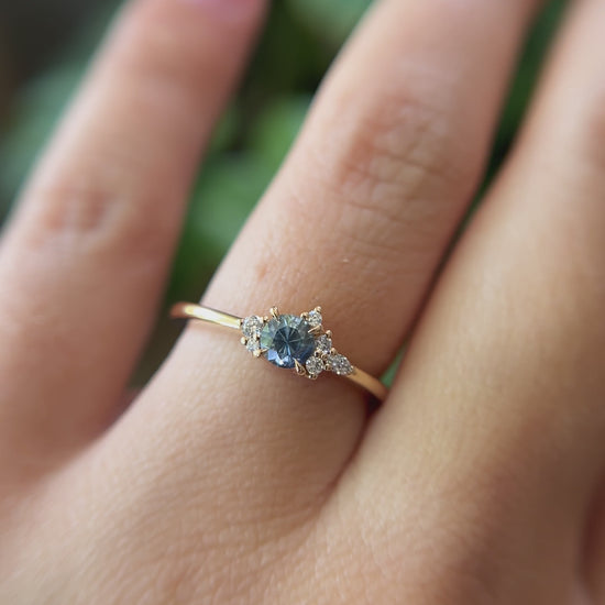 0.39ct round blue-teal sapphire and natural diamond constellation engagement ring in 14k yellow gold, worn on finger showing gemstone colour and diamond cluster detail