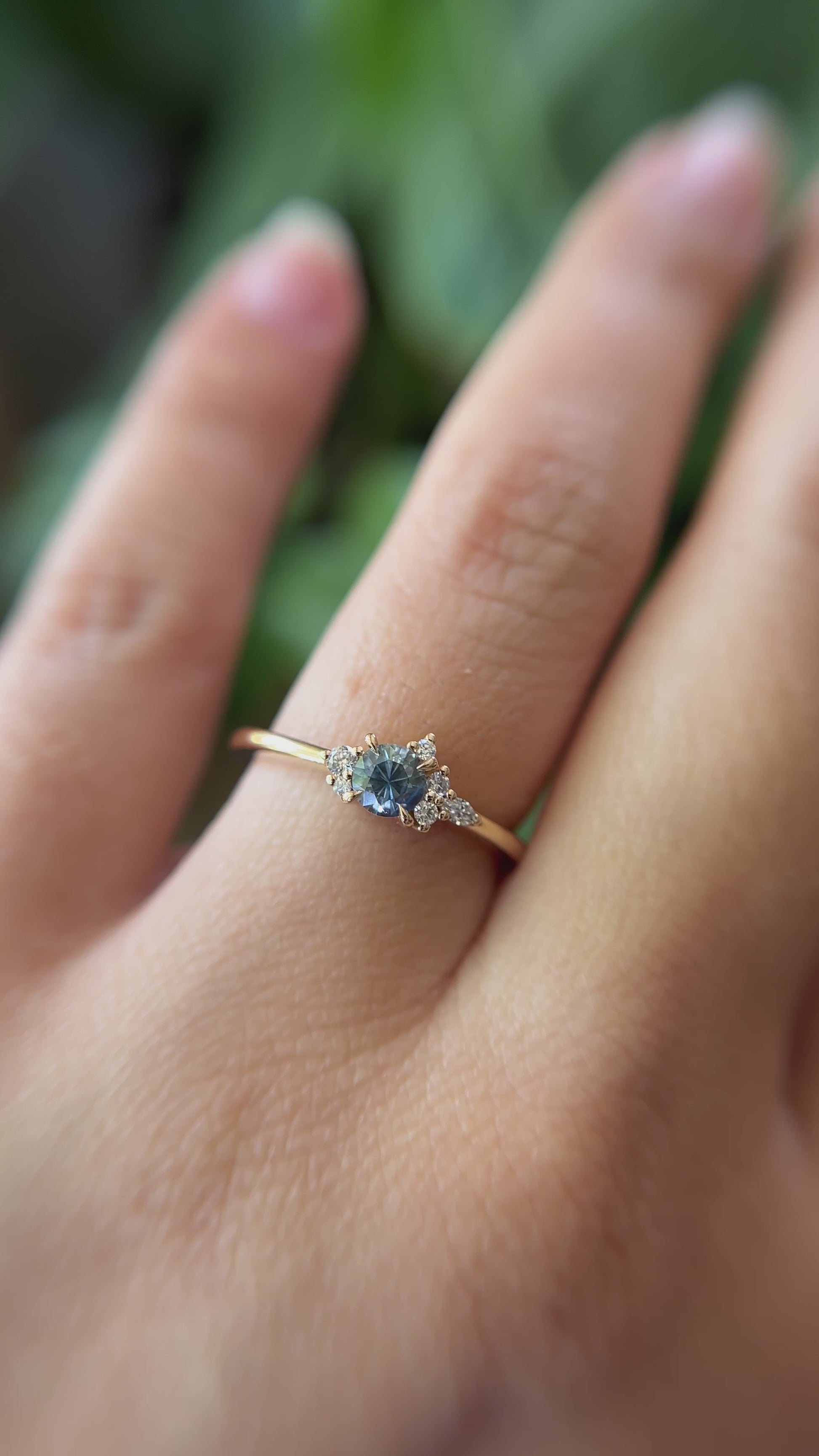 0.39ct round blue-teal sapphire and natural diamond constellation engagement ring in 14k yellow gold, worn on finger showing gemstone colour and diamond cluster detail