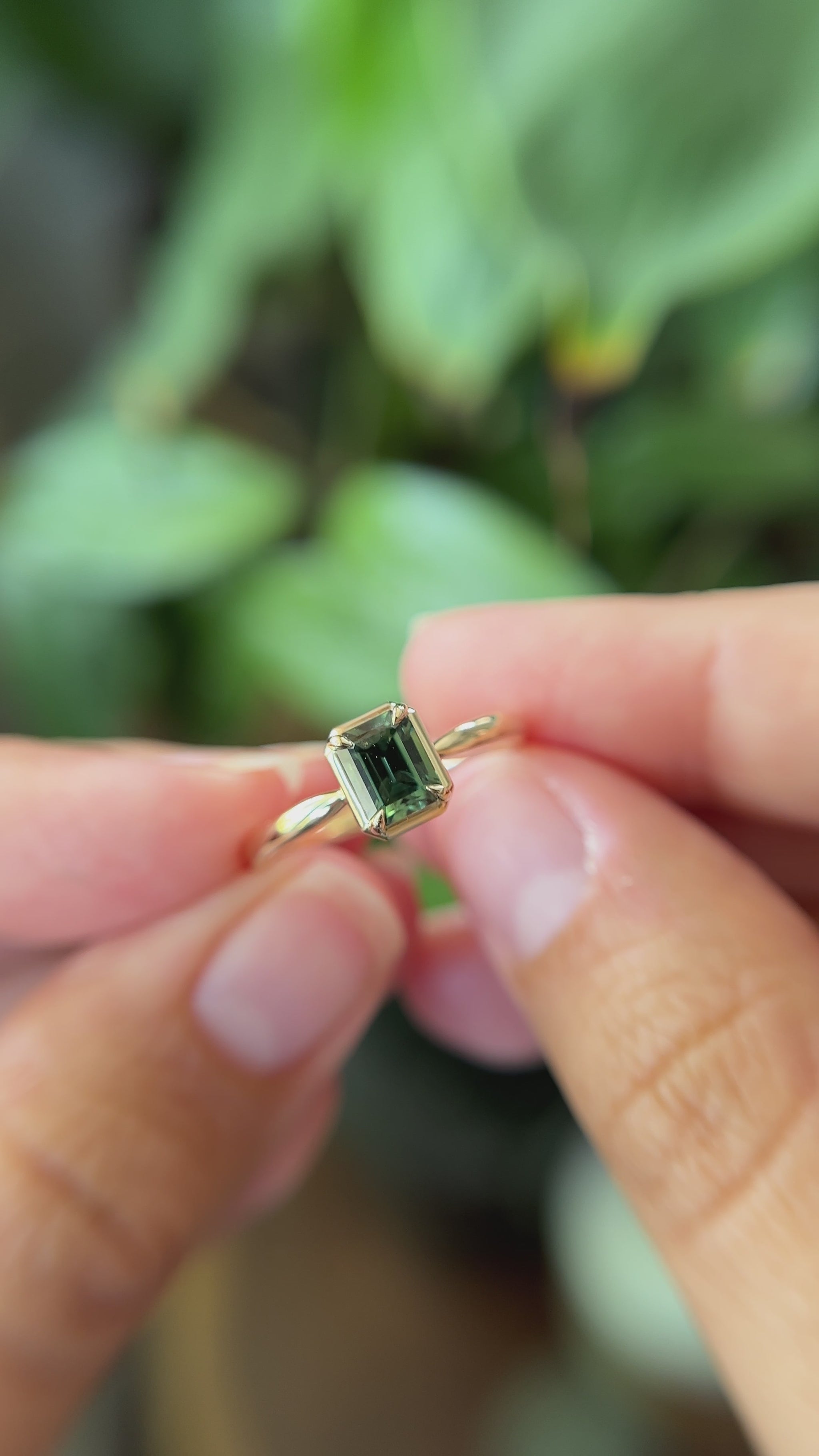 1.05ct emerald-cut forest green Madagascar sapphire solitaire engagement ring in 14k yellow gold, held in hands showing gemstone colour and faceting