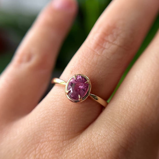 1.20ct oval orangy-pink sapphire solitaire engagement ring in 14k yellow gold with gold frame eagle-claw setting, worn on finger showing gemstone colour and movement