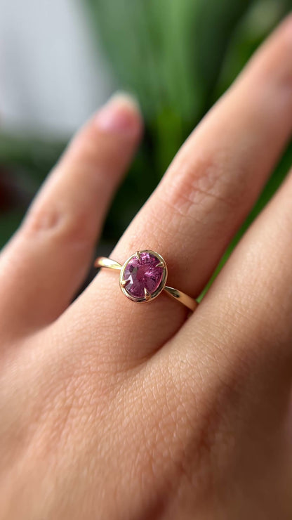 1.20ct oval orangy-pink sapphire solitaire engagement ring in 14k yellow gold with gold frame eagle-claw setting, worn on finger showing gemstone colour and movement