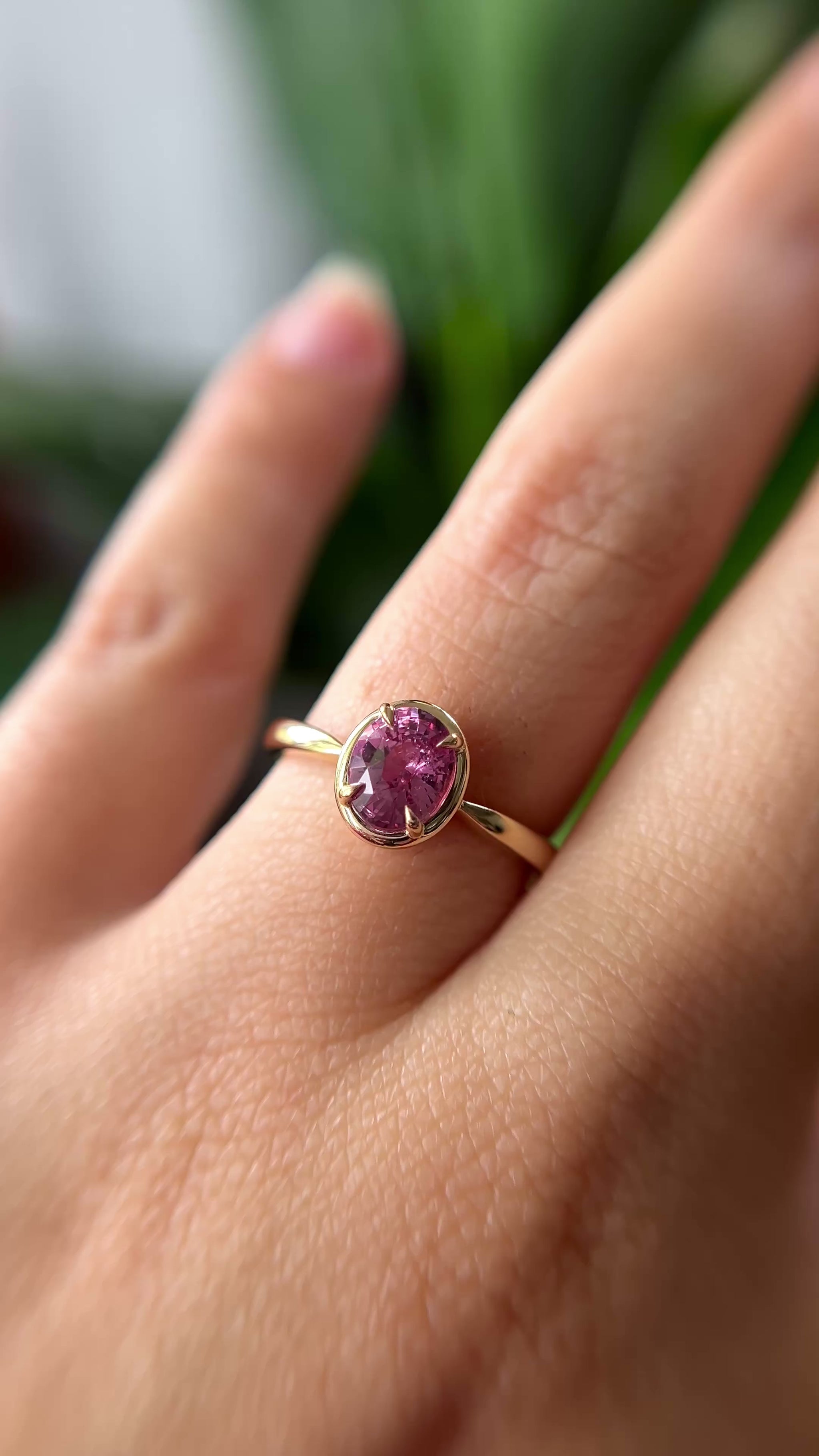 1.20ct oval orangy-pink sapphire solitaire engagement ring in 14k yellow gold with gold frame eagle-claw setting, worn on finger showing gemstone colour and movement