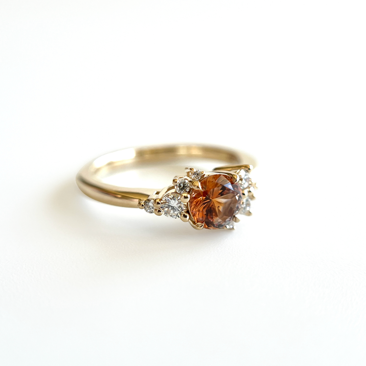 Bague de fiançailles en saphir Montana orange-rose et diamants en or jaune 14k, vue en angle montrant le serti asymétrique