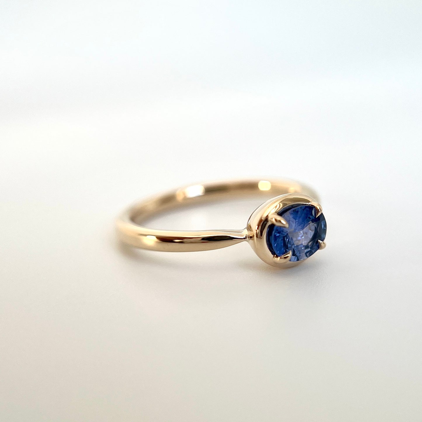 0.61ct unheated oval royal blue sapphire solitaire ring in 14k yellow gold, angled view showing gold frame setting and band detail