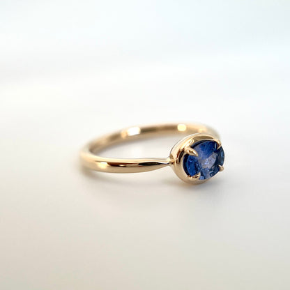0.61ct unheated oval royal blue sapphire solitaire ring in 14k yellow gold, angled view showing gold frame setting and band detail
