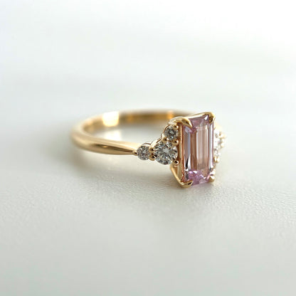 Side view of a 14k yellow gold ring, with an eagle-claw set emerald-cut light pink sapphire and diamond accents. The photo focuses on the setting details on the 3 round side diamonds on the left. 