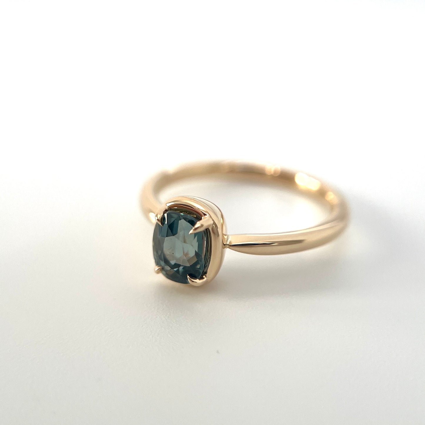 1.10ct elongated cushion cut teal sapphire solitaire ring in 14k yellow gold, angled view showing gold frame setting and band detail