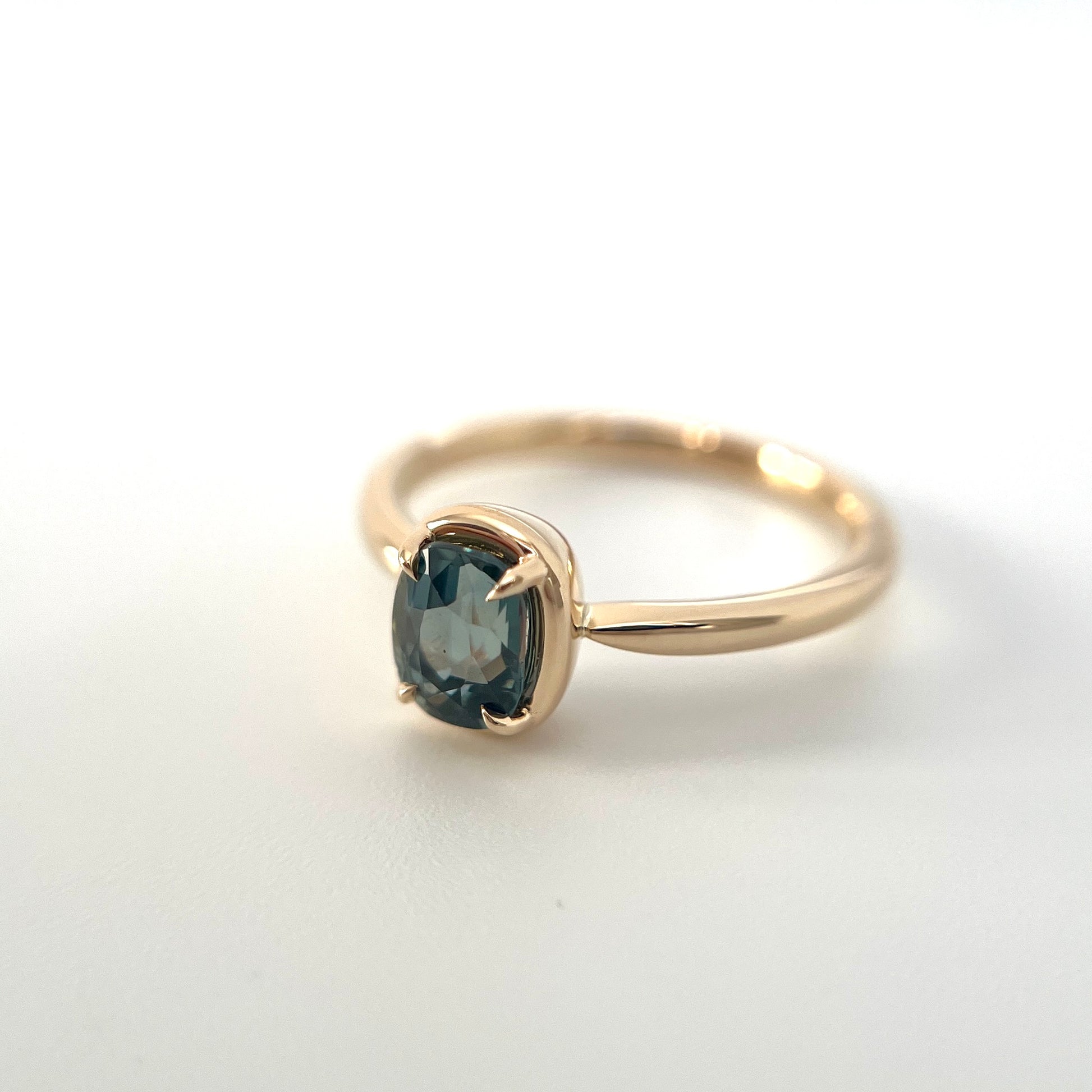 1.10ct elongated cushion cut teal sapphire solitaire ring in 14k yellow gold, angled view showing gold frame setting and band detail