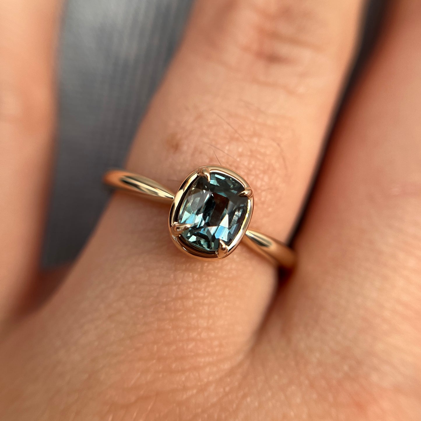 1.10ct elongated cushion cut teal sapphire solitaire ring in 14k yellow gold, worn on hand showing stone colour and setting detail