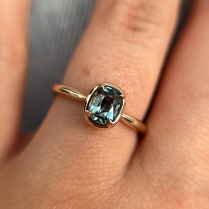 1.10ct elongated cushion cut teal sapphire solitaire ring in 14k yellow gold, worn on hand showing stone colour and setting detail
