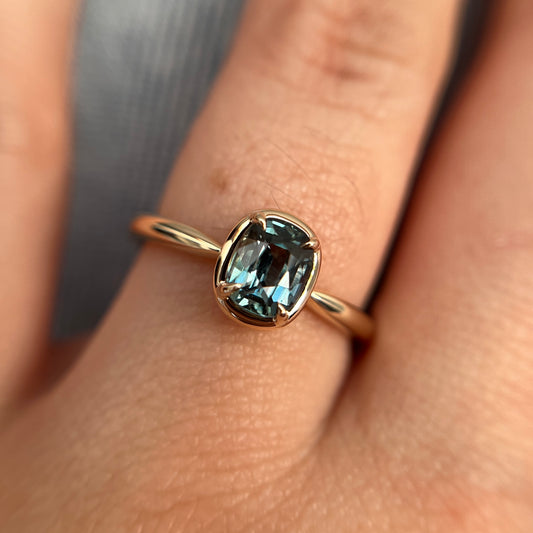 1.10ct elongated cushion cut teal sapphire solitaire ring in 14k yellow gold, worn on hand showing stone colour and setting detail