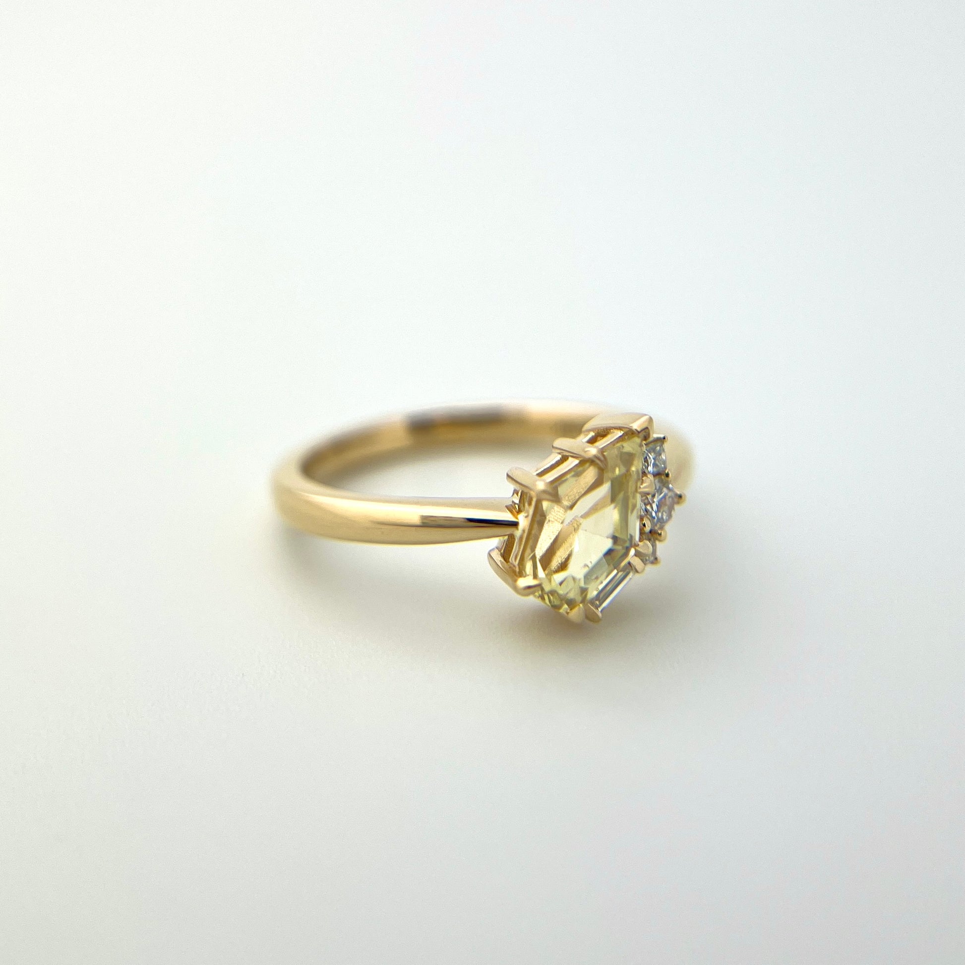 1.07ct shield cut light yellow Sri Lankan sapphire and diamond ring in 18k yellow gold, angled view showing eagle claw setting and band detail