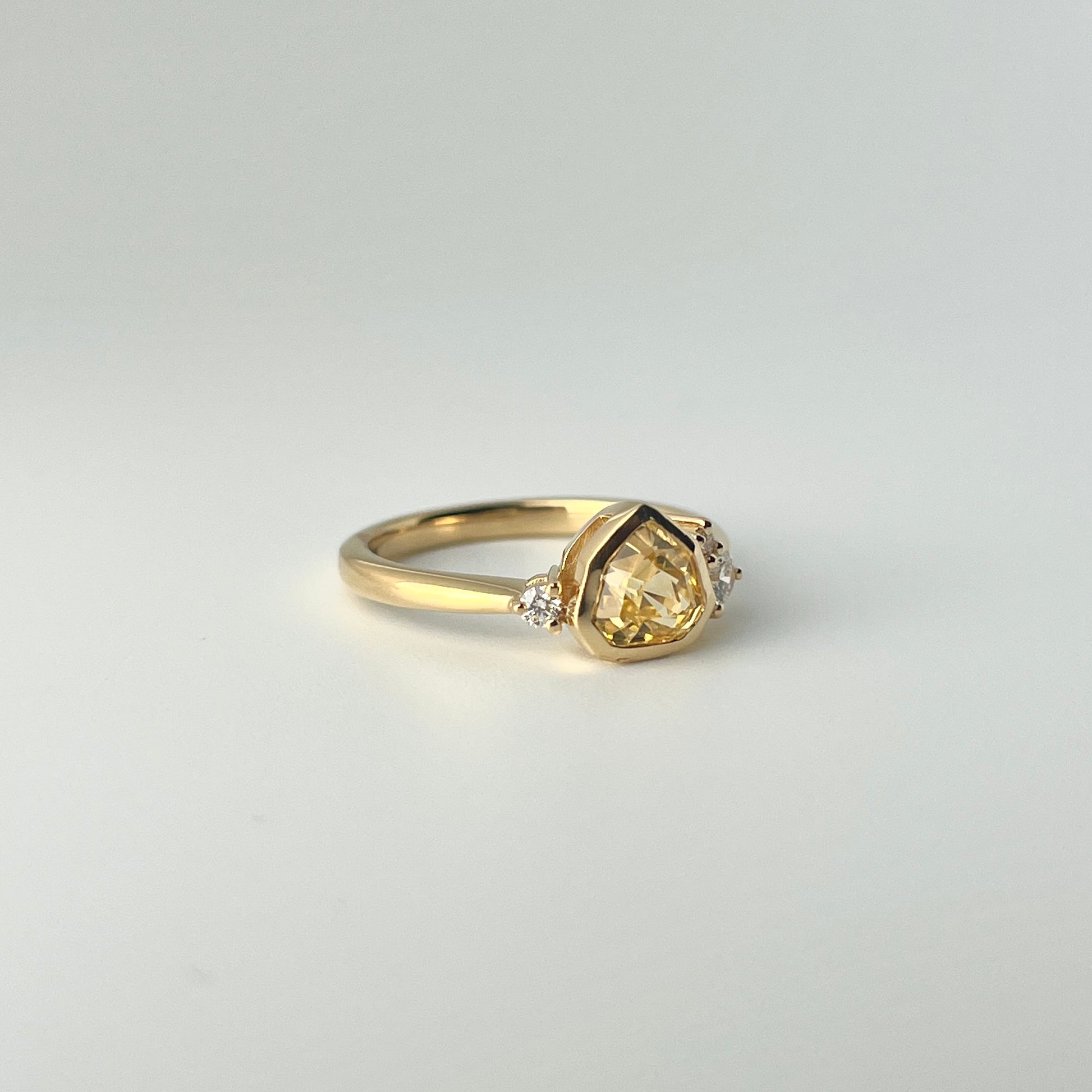 1.18ct mixed-cut trillion shaped bright yellow Sri Lankan sapphire and diamond ring in 18k yellow gold, angled view showing bezel setting and band detail